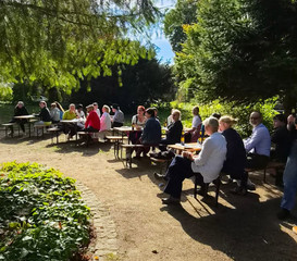 Mitarbeitenden sitzen beim Oktoberfest der Immanuel Klinik Märkische Schweiz bei strahlendem Sonnenschein im Park auf Bierbänken