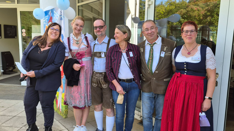Mitarbeitende stehen zum Teil in bayerischer Tracht vor dem Eingang der Immanuel Klinik Märkische Schweiz 